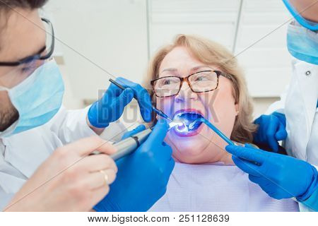 Dentists hardening toot crown with UV light treating senior patient 