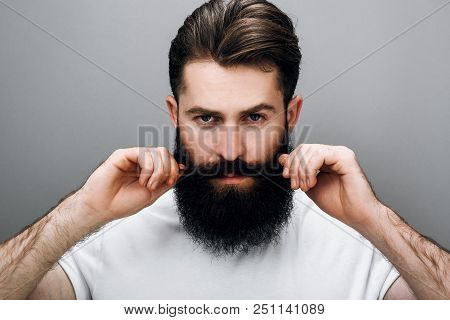 Horizontal Close Up Portrait Of Brutal Handsome Young Bearded Male Corrects His Moustache And Beard,