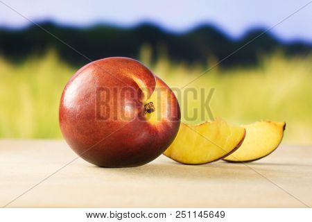 Group Of One Whole Two Slices Of Ripe Deep Red Nectarine With Green Wheat Field In Background