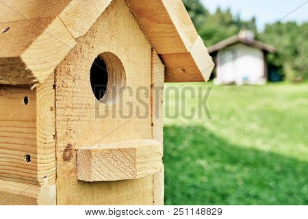 Wooden Birdhouse Close-up On The Foreground With A Summer House On The Blurred Background