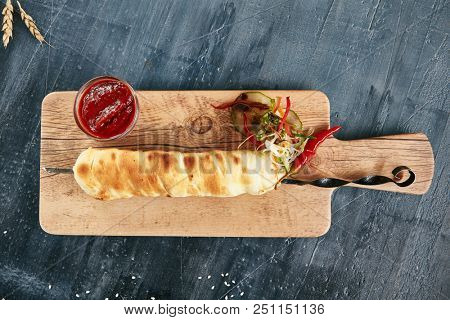 Grilled Khachapuri Made from a Delicious Tender Dough with Melted Burnt Imeretian Cheese Close Up on Rustic Wooden Background with Selective Focus. Traditional Long Bread on a Skewer Fried on Grill
