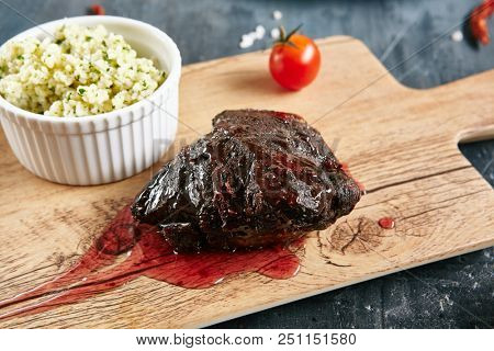 Beef Cheeks with Red Berry Sauce and Couscous Close Up. Hot Grilled Veal Tenderloin on Rustic Wooden Background with Spices and Garnish of Wheat Grains