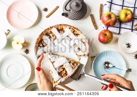 Homemade Apple Pie Sprinkled With Powdered Sugar In Female Hand On A White Table Next To Apples, Cin