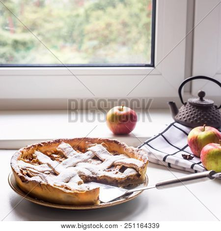 Homemade Apple Pie Sprinkled With Powdered Sugar In Female Hand On A White Table Next To Apples, Cin