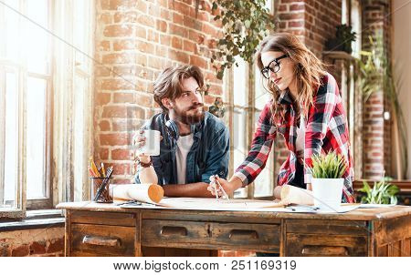 Female Ambitious Architect In Glasses Showing An Architectural Plan To Her Young Bearded Co-worker A
