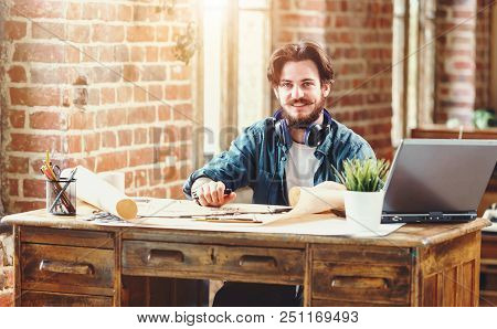 Handsome Bearded Male Architect Working On A Building Plan At His Desk Smiling To The Camera Joyfull