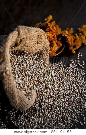 Close Up Of Raw  Dried Grains Of Pearl Millet With Jaggery Or Gud On A Wooden Surface In Drak Gothic