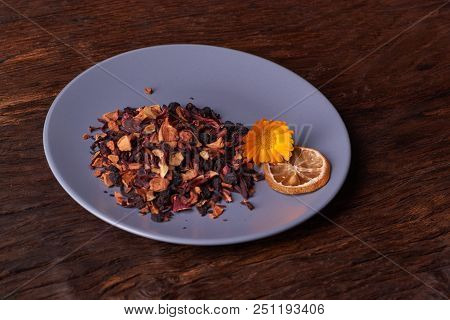 Black Dry Fruit Tea Leaves In Blue Plate On Wooden Table