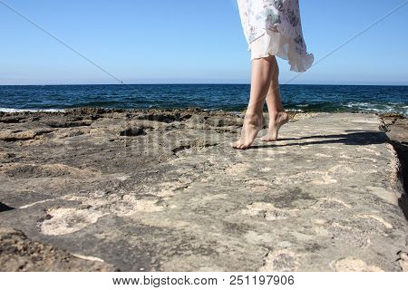 Legs Of Young Girl In White Fluttering Skirt Stand Tiptoe On Stone Beach
