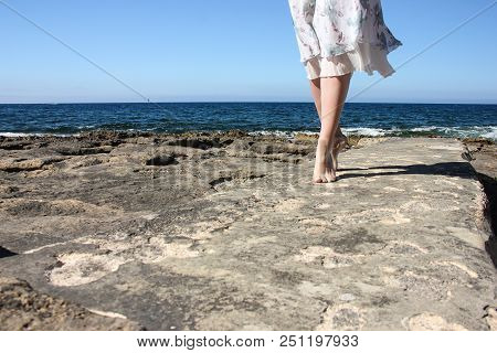 Legs Of Young Girl In White Fluttering Skirt Stand Tiptoe On Stone Beach