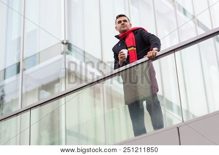 Content Dreamy Young Man With Coffee Cup Looking Into Distance And Leaning On Railing. Below View Of