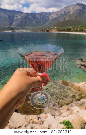 A Glass Of Red Martini In The Woman Hand On The Background Of A Picturesque Seascape, Summer Vacatio
