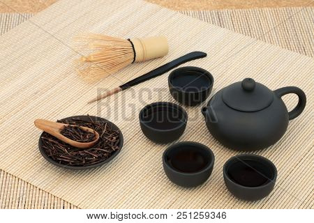 Japanese kuchika roasted twig green tea with teapot and cups, stirrer and whisk on bamboo background. Has many health benefits including rejuvenating properties.