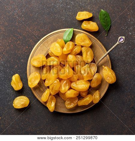 Dried Yellow Kumquat With Green Leaves On Brown Background. Top View.