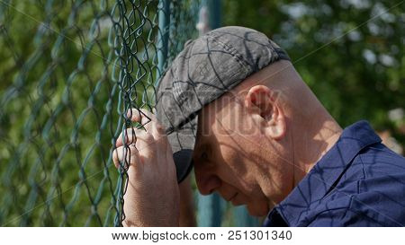 Disillusioned And Hopeless Man Hanging With Hands On Metallic Fence