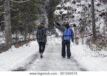 Young Couple Guy And Girl Walking In The Snow-covered Forest Among The Rocks