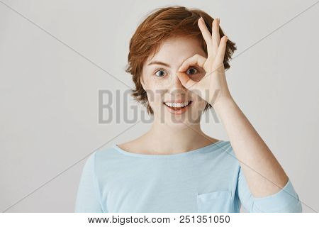 Excited Good-looking Redhead Girl With Freckles Making Okay Or Fine Gesture Over Eye As If It Is Mon