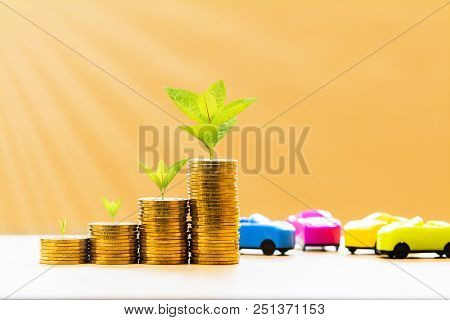 Car Model And Stack Coin With Plant Growing On The Top For Collect Interest Put On The Desk In The O