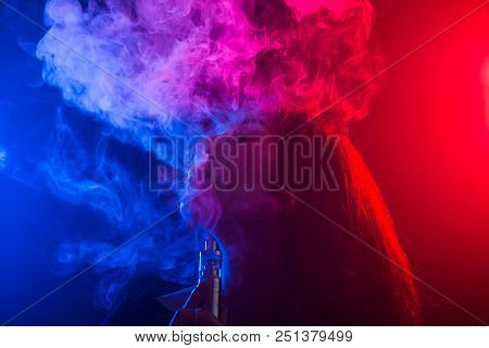 Portrait Of Young Woman In Neon Red And Blue Smoke With Vape Or E-cigarettes.