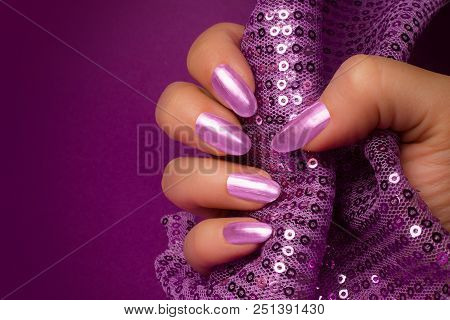 Female Hand With Shiny Purple Nails Is Holding Purple Glittered Fabric On Purple Background, Nail Ca