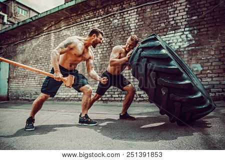 Two Muscular Athletes Training. Muscular Fitness Shirtless Man Moving Large Tire Other Motivate Him 