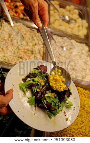 Self-service Restaurant Customer Serves With A Spoon And Puts Lettuce And Corn In The Dish