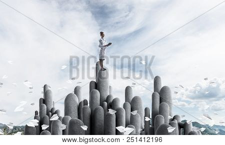 Young Female Doctor With Folder In Hands Satnding On Stone Column