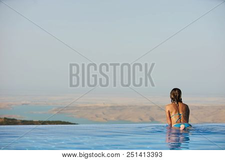 Young Woman Relaxaing In The Swimming Pool Looking At The Nature Landscape View On Background. Trave