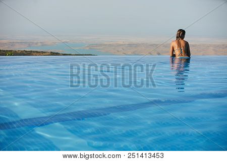 Young Woman Relaxaing In The Swimming Pool Looking At The Nature Landscape View On Background. Trave