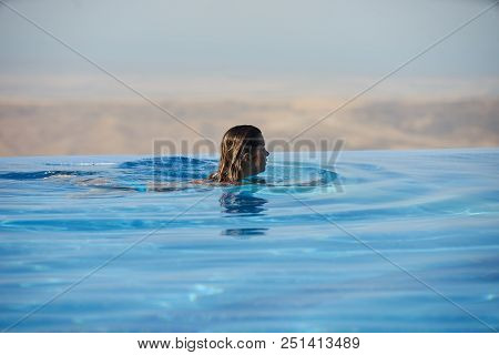 Young Woman Relaxaing In The Swimming Pool Looking At The Nature Landscape View On Background. Trave