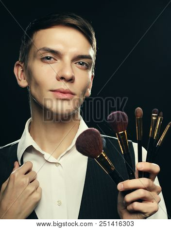 Ready to do make up. Young male make up artist posing with make-up brushes on a dark background