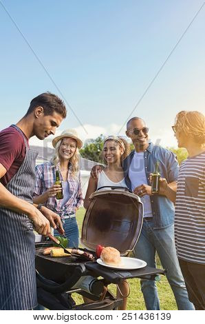 Group of multiethnic young friends enjoying barbecue in the backyard. Happy men and beautiful women talking and grilling meat. Smiling guys and girls having a good time at outdoor party.