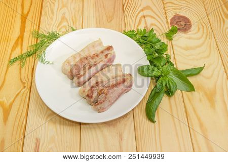Two Slices Of The Grilled Streaky Bacon On The White Dish And Different Greens On A Wooden Surface