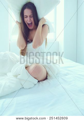 Young caucasian woman covering her head and ears with pillows.