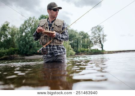 A Picture Of Man Holding Box With Flies And Plastic Artificial Baits. He Is Holding One Of Them In H