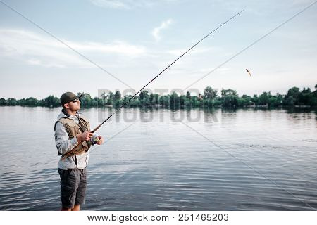 A Picture Of Fishaerman Standing In Shallow And Fishing. He Holds Fly Rod. Guy Looks Up And Forward.