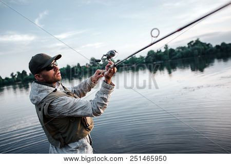 Fisherman In Action. He Holds Fly Rod Witth Both Hands. Guy Is Trying To Catch Salmon. He Is Serious