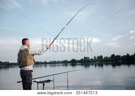 Fisherman Is Standing Near Watr And Holding Fly Rod With Right Hand. He Has It Up Really High. Man L
