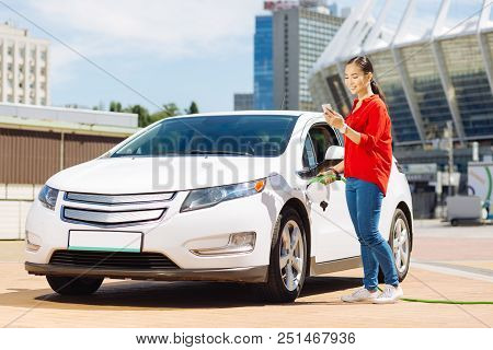 Car Fuel. Attractive Asian Woman Standing Near Her Car While Fuelling It