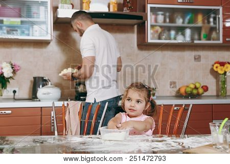 Little Kid Girl Plays With Flour While Daddy Cooking In Kitchen At Table. Happy Family Dad, Child Da