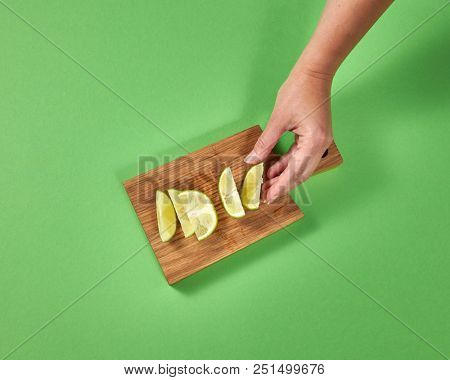 Organic natural fresh lime slices on a wooden board. Female hands takes a piece of lime for preparing homemade natural lemonade. Concept of healthy natural vegetarian food.