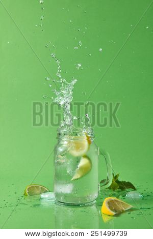 Ice cubes falling in lemonade with splashes and drops isolated on green background. Slices of citrus fruits, ice pieces, mint on a green table.