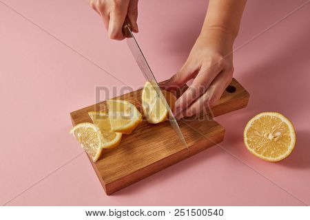 Woman cutting organic yellow ripe lemon with steel knife on pink for preparation detox drink for dietary healthy food. Concept vegetarian food.