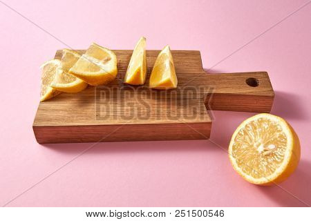 Juicy slices and half of ripe yellow lemon on a wooden brown board on a pink . Healthy food concept.