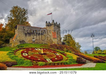Picturesque View To Former Royal Castle In Nowy Sacz, Poland At Autumn Day. Colorful Flower Clock On
