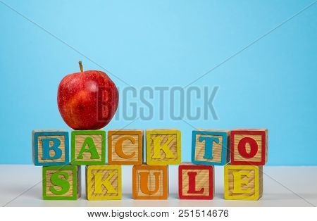 Stack Of Wooden Blocks Wrongly Spelling Back To School With Red Apple On Top Against Blue Background