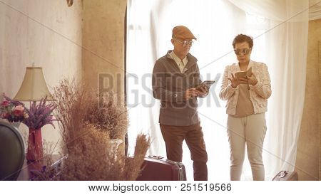 Asian Senior Couple Use Smart Phone Technology While Travel With Suitcases In Luxury Interior