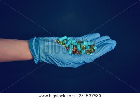 A Hand In A Blue Medical Glove Holds Medications And Pills Of Different Colors On A Black Background