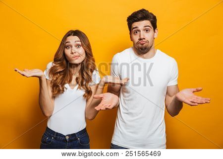 Image of happy young people man and woman in basic clothing throwing up arms with puzzlement isolated over yellow background