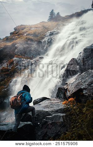 Traveler With A Backpack Climbing On A Mountain Near A Waterfall.